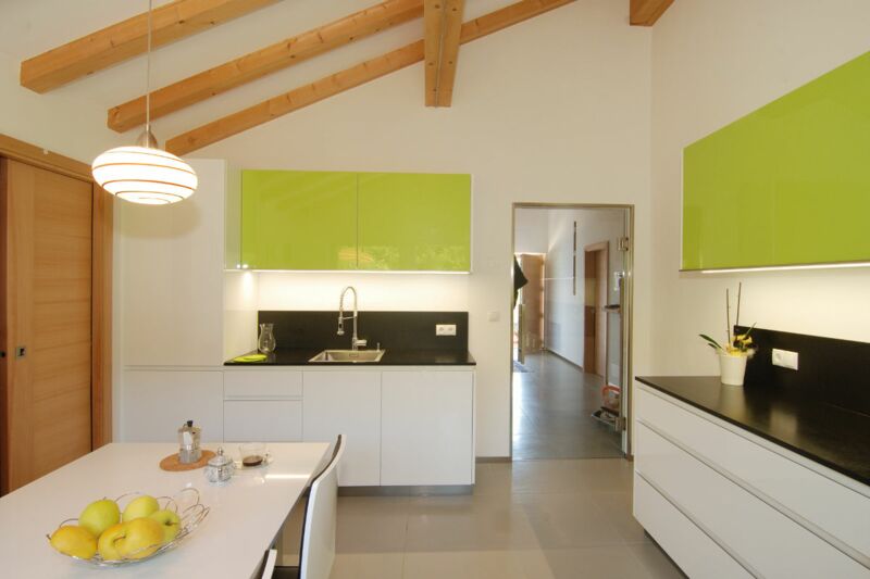 Küche in weissem Hochglanz, kombiniert mit Fronten in zartem "Yellow-Green" und Arbeitsplatten in schwarzem Granit